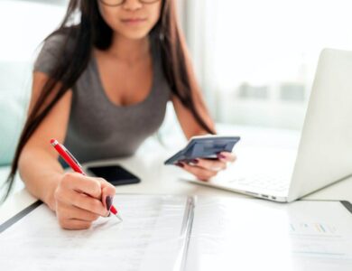 Asian woman using calculator and laptop for calaulating home budget finance taxes