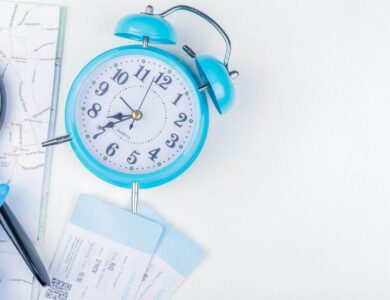 top view of blue alarm clock with magnifying glass blue toy plane and plane tickets on a map