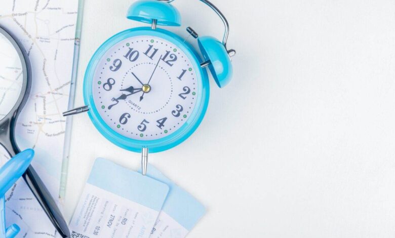 top view of blue alarm clock with magnifying glass blue toy plane and plane tickets on a map