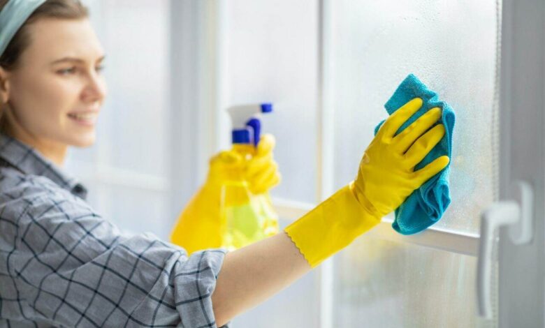 Young housekeeper washing window glass with rag and spray detergent, selective focus